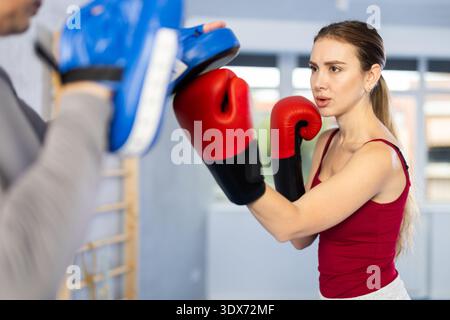 Una donna atletica impara a sbattere battendo guanti da pugno. Donna con il suo allenatore in palestra Foto Stock