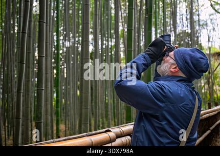 Uomo barbuto anziano in berretto che fotografa il boschetto di bambù di arashiyama, Kyoto, Giappone Foto Stock