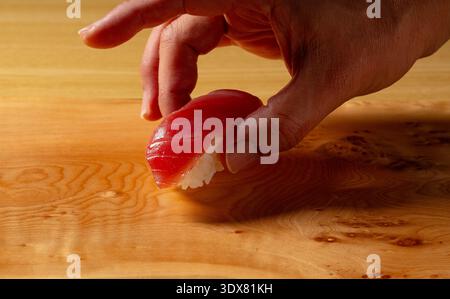Raccogliere a mano il maguro (tonno) nigiri fresco da un tavolo di legno Foto Stock