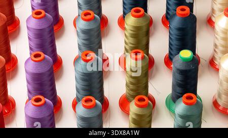 Bobine colorate di filetto disposte ordinatamente in fila per i progetti di cucitura Foto Stock