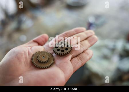 Persona che tiene la mano un piccolo ingranaggio metallico arrugginito e una ruota dentata. Queste parti di un orologio antico di una vecchia macchina evocano una nostalgica sensazione di scoperta e di Foto Stock
