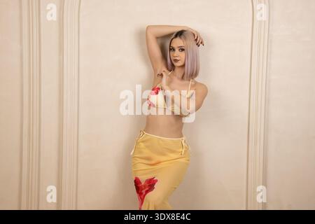 Donna alla moda in abiti gialli in posa con le mani sulla testa Foto Stock