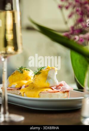 Una vista dall'alto su due uova perfettamente cotte servite su muffin inglesi con prosciutto a fette, abbondantemente condite con salsa gialla Hollandaise e fr Foto Stock