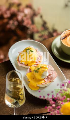 Una vista dall'alto su due uova perfettamente cotte servite su muffin inglesi con prosciutto a fette, abbondantemente condite con salsa gialla Hollandaise e fr Foto Stock