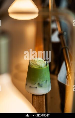 Un rinfrescante latte matcha ghiacciato con strati distinti di latte e vivace tè verde, condito con una ricca schiuma cremosa o una paletta di gelato. Foto Stock