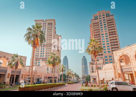 30 novembre 2025, Doha, Qatar: Architettura moderna che costeggia una strada con alte palme e residenze di lusso nella perla Foto Stock