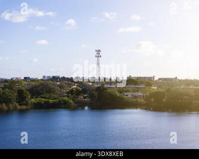 Vista aerea di una torre di telefoni cellulari che si innalza sopra il paesaggio della città, il suo metallo scuro che contrasta con i lussureggianti verdi e blu che si riflettono sotto una tela Foto Stock