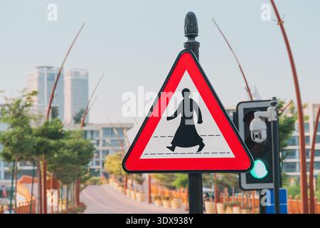 Cartello di attraversamento pedonale che mostra una persona in abito tradizionale arabo, accanto a un semaforo verde e a una telecamera di sorveglianza Foto Stock