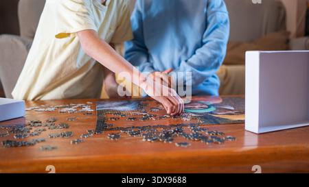 I bambini stanno posizionando con cura pezzi di puzzle su un tavolo di legno, godendo di tempo libero attivo Foto Stock