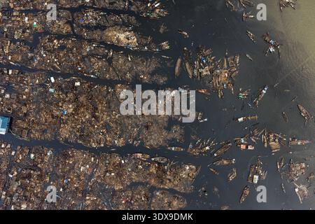 Vista aerea delle barche sparse attraverso le acque scure, che riflettono il cielo in mezzo al vasto insediamento di Lagos, Lagos, Nigeria. Foto Stock