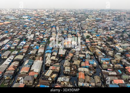 Vista aerea di un vasto insediamento dove gli edifici incontrano l'acqua, creando un arazzo di texture e toni sotto un cielo nebbioso, Lagos, Lagos, Nigeri Foto Stock