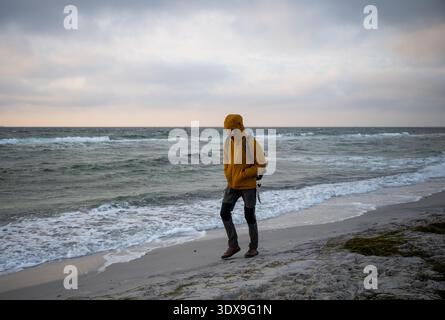 Uomo solitario che cammina lungo la spiaggia sabbiosa del Mar Baltico sotto il cielo nuvoloso Foto Stock