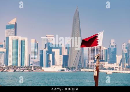 1 dicembre 2025, Doha, Qatar: Bandiera del Qatar che sventola contro il moderno skyline e gli alti edifici di West Bay Foto Stock