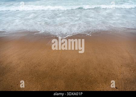 Le dolci onde dell'oceano bagnano una spiaggia sabbiosa di Barcellona in una giornata limpida Foto Stock