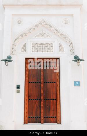 Elegante porta in legno caratterizzata da tradizionali intagli arabi e dettagli su una facciata bianca dell'edificio, che mostra un'architettura distintiva Foto Stock