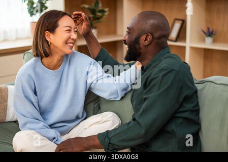 Due partner si coccolano su un divano, sorridendo brillantemente mentre si godono la compagnia l'uno dell'altro in un ambiente interno elegante e invitante. Foto Stock