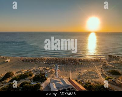 Vista aerea del sole che baciava il mare tranquillo mentre incontra la spiaggia sabbiosa di Phalasarna Beach, Chania, Grecia. Foto Stock