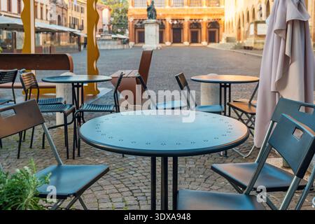 Tavoli e sedie da caffe' all'aperto si trovano su lastricati in Piazza Cavour, Rimini, Italia, con statua e storici edifici civici sullo sfondo Foto Stock