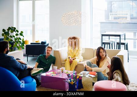 Un gruppo di professionisti di sesso maschile e femminile che parlano tra loro mentre si siedono nella hall dell'ufficio Foto Stock