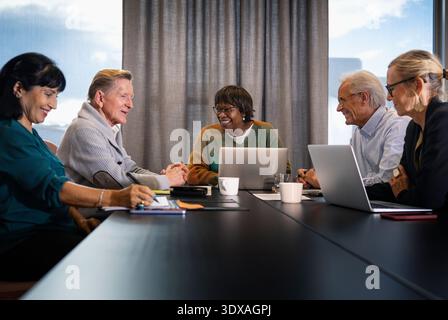Gruppo di imprenditori sorridenti seduti intorno al tavolo sul posto di lavoro Foto Stock
