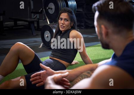 Donna che parla con un uomo seduto sul pavimento in palestra Foto Stock