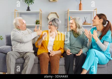 Felice sorridente anziani che giocano divertente gioco con la giovane infermiera amichevole in casa di riposo. Foto Stock