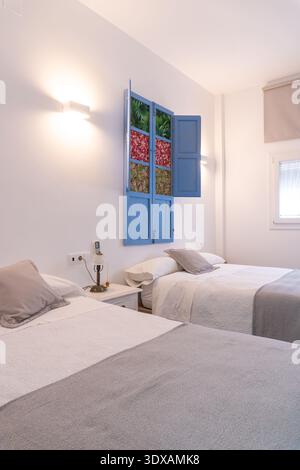 Interni luminosi e luminosi di una camera da letto dotata di due letti singoli con biancheria bianca, getti grigi e decorazioni delle finestre Foto Stock