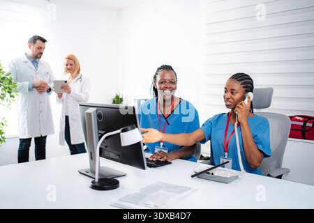 Personale sanitario che collabora presso la clinica medica utilizzando computer e telefono Foto Stock