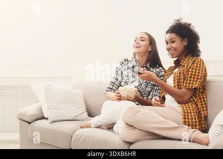 Gli amici possono guardare film insieme mentre sono seduti sul divano con spuntini e telecomando Foto Stock