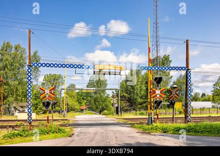 Strada di campagna che attraversa una ferrovia a un passaggio a livello con segnali e cancelli a sbarra Foto Stock