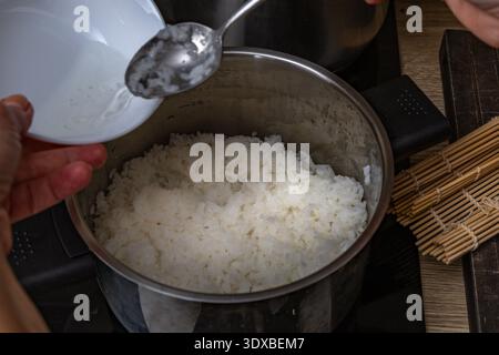Versare l'aceto di riso in una pentola di riso, aggiungere zucchero, ingredienti per il sushi, riso cinese bianco in una pentola, preparare il sushi a casa, una ricetta fatta in casa Foto Stock