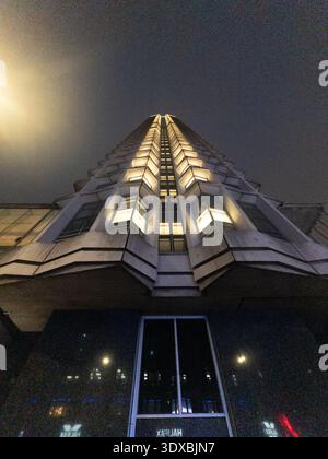 Vista notturna dall'angolo basso della torre illuminata Centre Point di Londra, facciata brutalista angolare in cemento con finestre luminose contro il cielo scuro Foto Stock