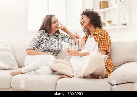 Due amici si divertono a stare insieme su un divano mentre condividono un dispositivo in un accogliente ambiente interno Foto Stock