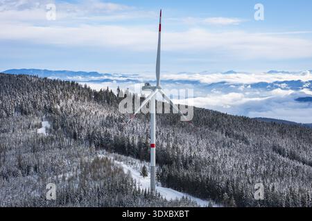 La vista aerea di una turbina eolica solitaria si erge in mezzo alla foresta piena di neve, raggiungendo il cielo nuvoloso, una testimonianza dell'energia rinnovabile, SOB Foto Stock