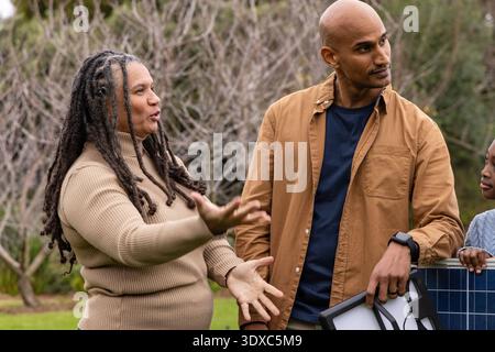 Famiglia afroamericana in piedi nel cortile, gesti donna, uomo che tiene il pannello incorniciato, bambino che tocca Foto Stock