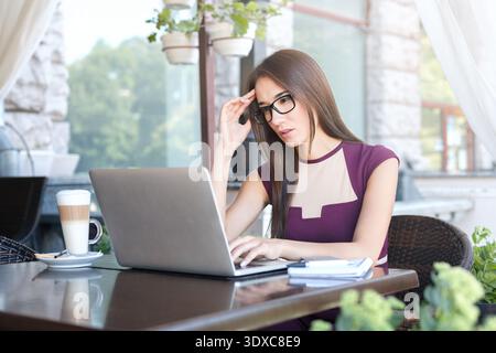 Donna che lavora su un laptop in Coffee Shop con una collezione di piante sullo sfondo Foto Stock