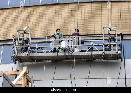 Montreal, Canada - 4 luglio 2025: Pulitori professionisti che lavorano su facciate alte. Personale addetto alla manutenzione su supporto per ponteggi sospeso. Lavavetri accesi Foto Stock
