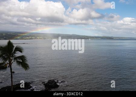 Guardando attraverso la baia di Hilo fino alle rive di Mauna Kea, uno splendido arcobaleno si estende attraverso l'acqua tropicale. Foto Stock