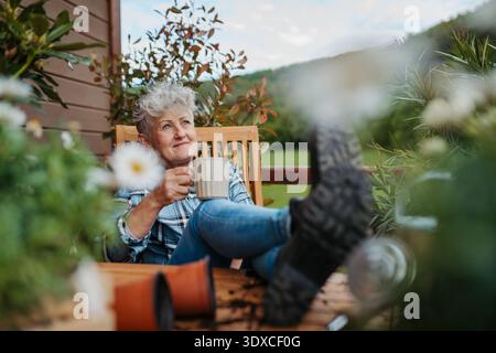 Donna anziana con caffè seduto in terrazza, riposante dopo il giardinaggio. Foto Stock
