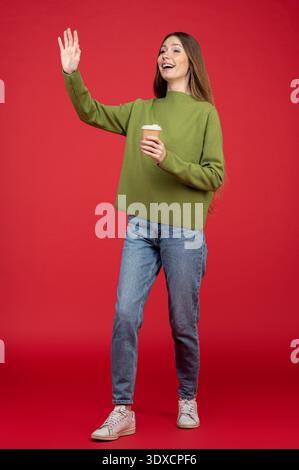 Giovane donna eccitata su sfondo rosso che sventolava la mano Foto Stock