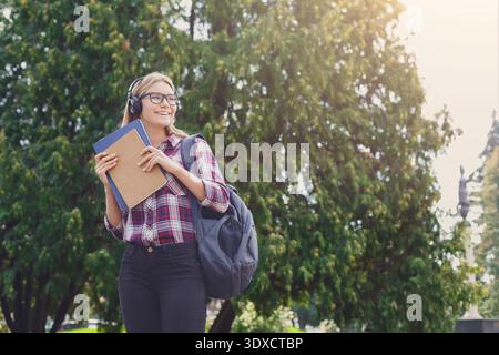 Gli studenti amano trascorrere una giornata di sole all'aperto mentre ascoltano musica e tengono in mano un notebook Foto Stock