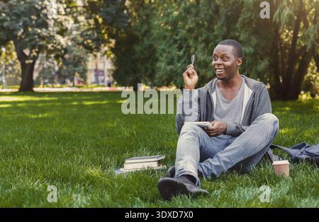 I giovani amano studiare nel parco tenendo in mano una penna e sorridendo Foto Stock