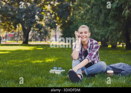 Giornata di sole nel parco con un giovane seduto sull'erba e godendo del tempo libero Foto Stock