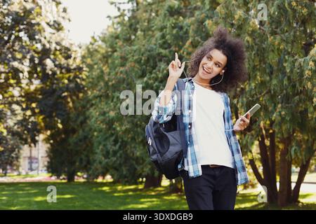 Giovani che si godono la musica all'aperto mentre sono in piedi nel Green Park durante la giornata di sole con zaino Foto Stock