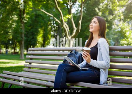 I giovani amano trascorrere il tempo a Park con caffè e tablet seduti sulla panchina durante la stagione soleggiata Foto Stock