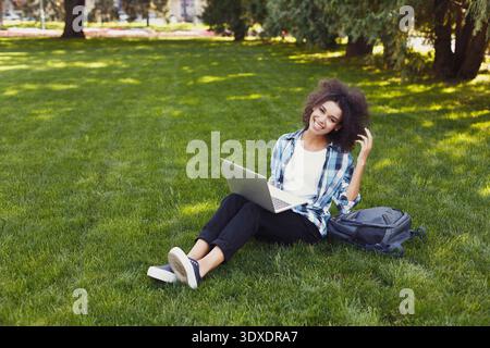 Giovane donna adulta che lavora su un laptop nel parco il giorno della domenica, si diverte all'aperto e si connette Foto Stock