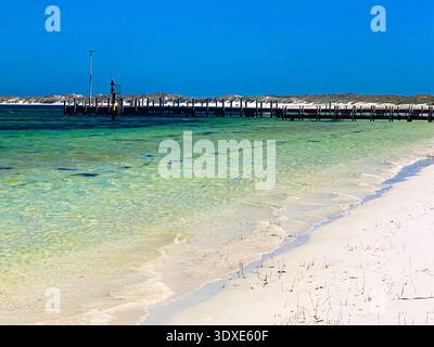 Un lungo molo di legno si estende nell'oceano, circondato da una spiaggia di sabbia e da acque cristalline, evocando serenità e relax. Foto Stock