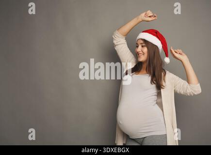 Le donne incinte che indossano un cappello di Babbo Natale si godono momenti di festa in uno studio durante le festività Foto Stock