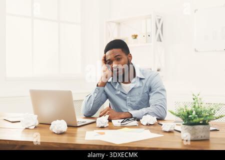 L'uomo che lavora si sente stressato in uno spazio luminoso per ufficio con sfere di carta intorno alla scrivania Foto Stock