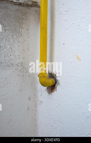 Primo piano di un tubo del gas in metallo verniciato giallo brillante con un giunto a gomito che scompare in un foro in una parete intonacata bianca testurizzata Foto Stock